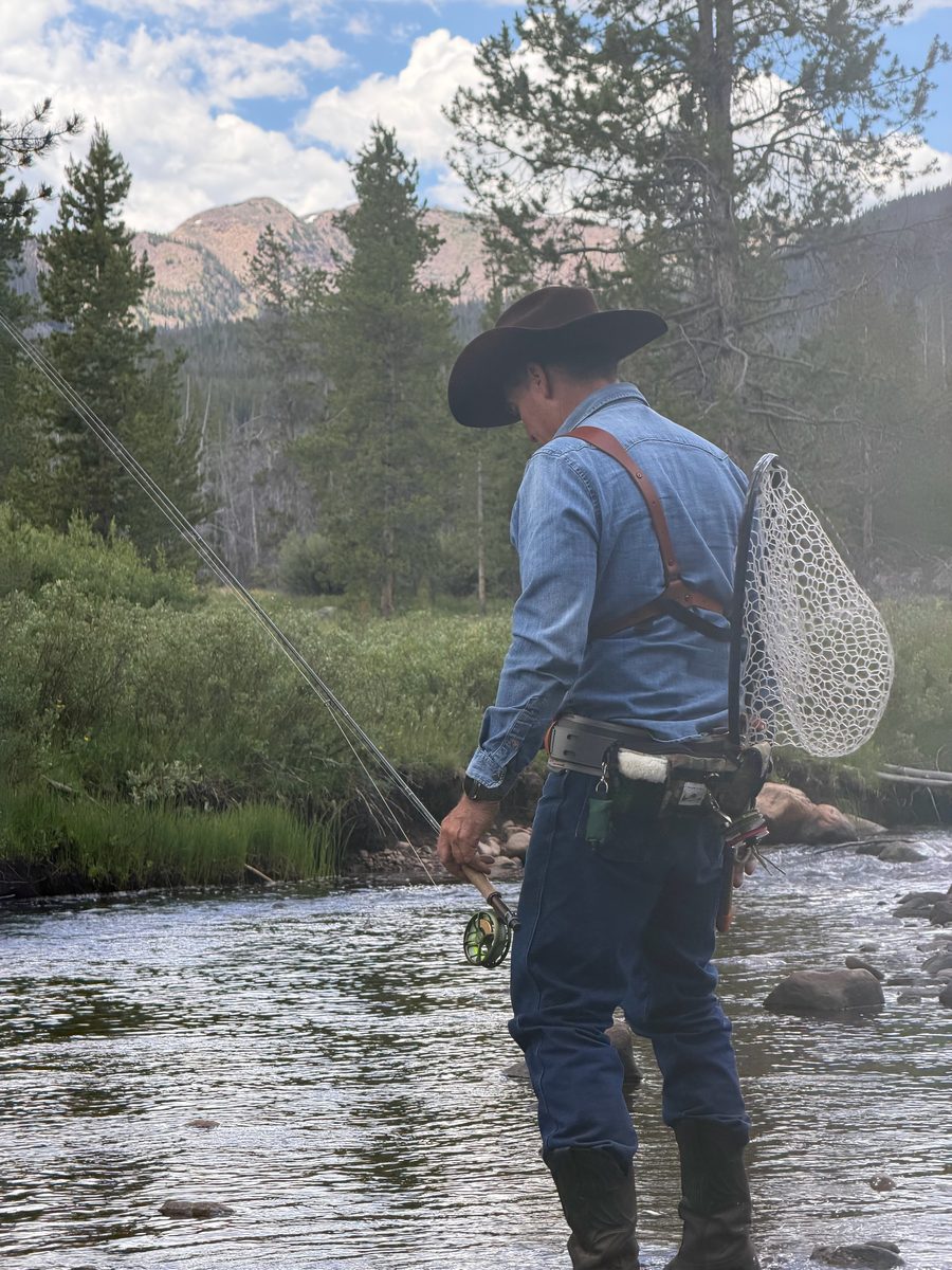 Fly fisher wading a mountain river with a net on his back
